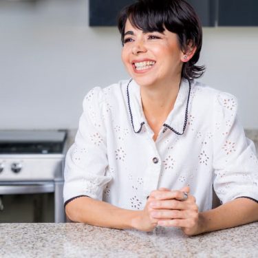 A cheerful woman leaning on a granite countertop in a modern kitchen.