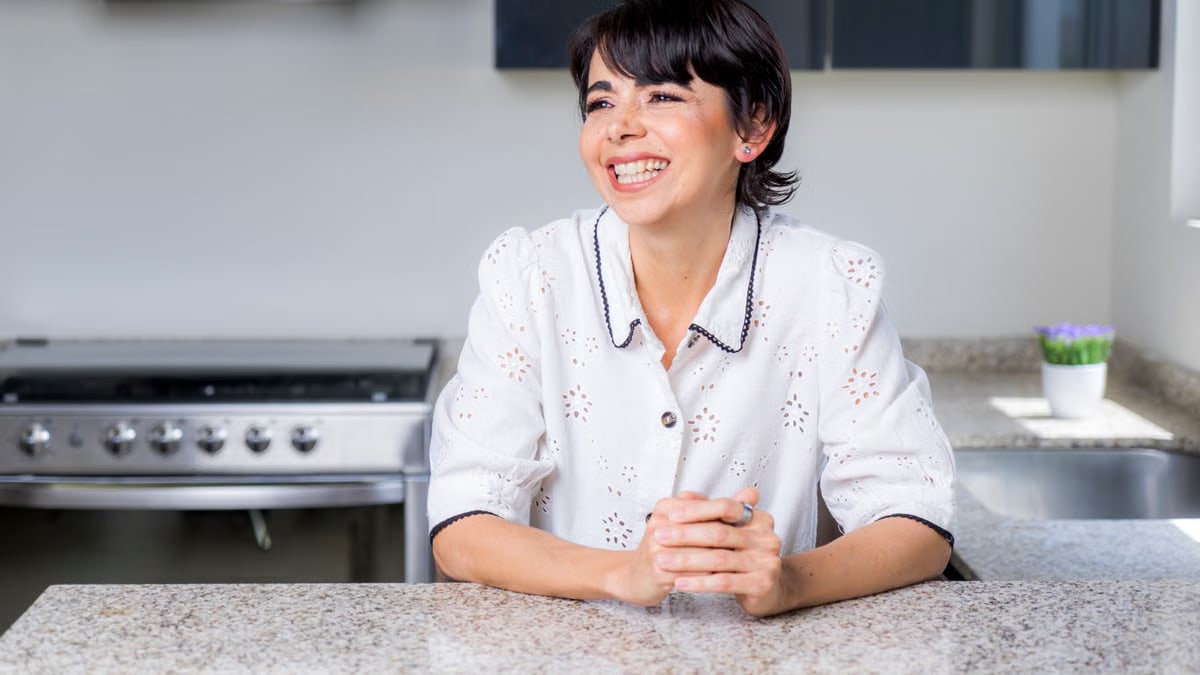 A cheerful woman leaning on a granite countertop in a modern kitchen.